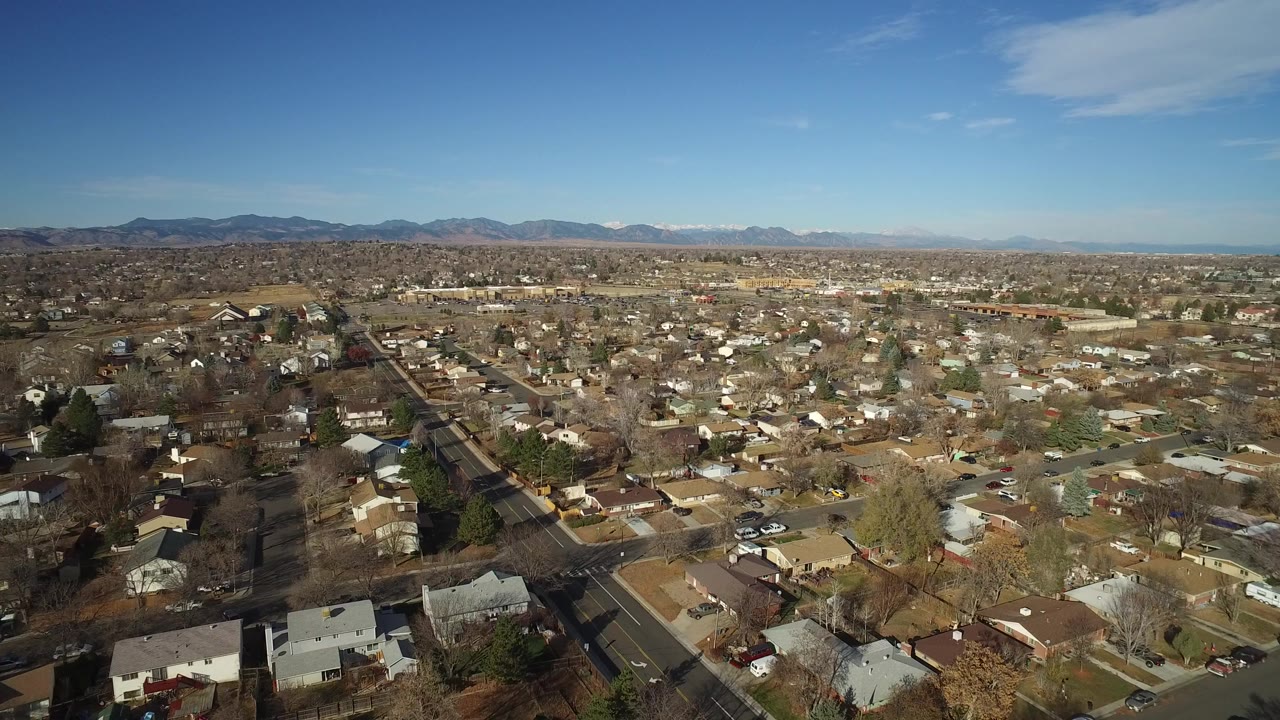 Aerial view of suburban homes, roads, trees, distant mountains, and blue sky.