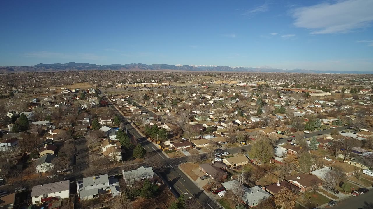Drone-height view across Westminster, Colorado residential blocks, with a straight road leading toward low mountains and no visible people.