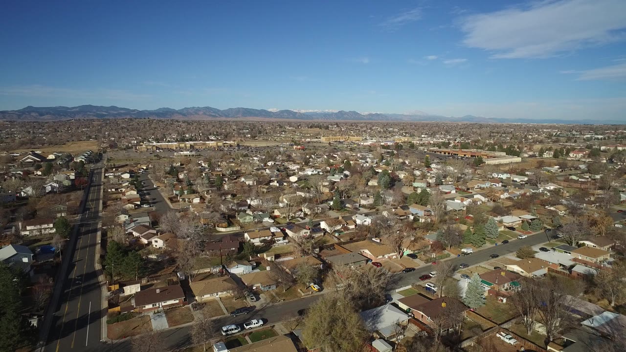 Aerial view over dense suburban homes and roads with mountains on the horizon.