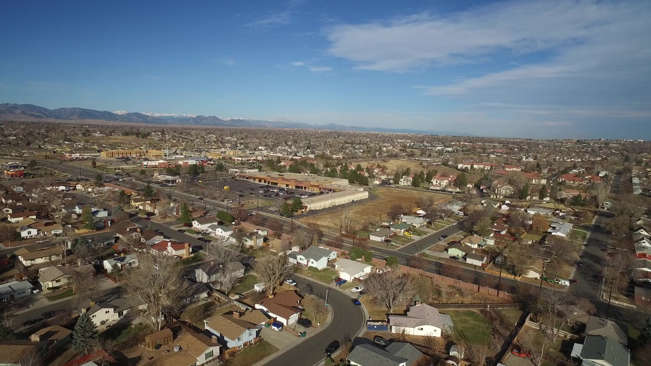 Drone-like aerial view of houses, streets, bare trees, and mountain horizon.