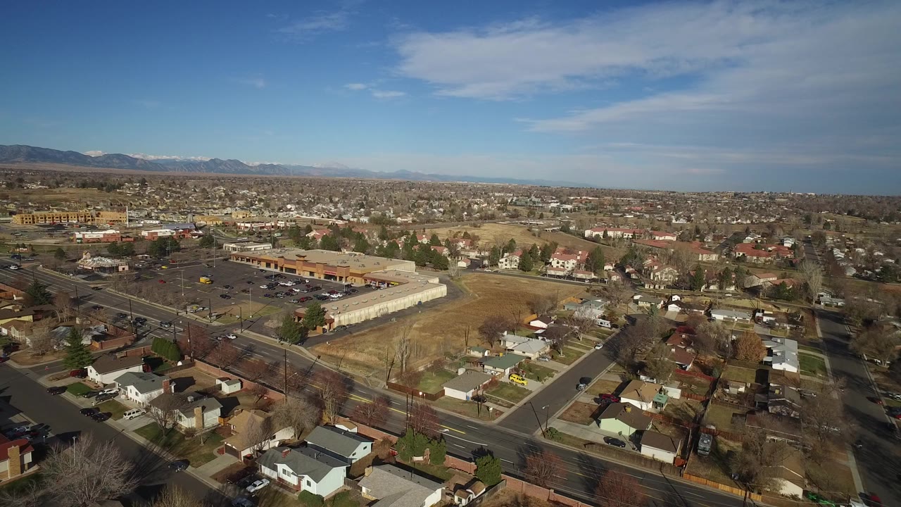 Aerial view over suburban houses, roads, retail buildings, and distant mountains.