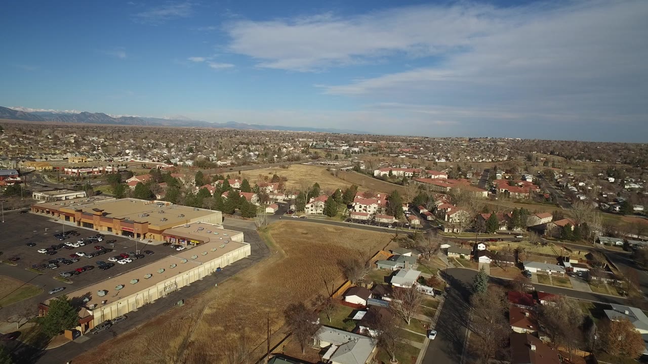 Suburban aerial view with a large low building, homes, dry land, and distant mountains.