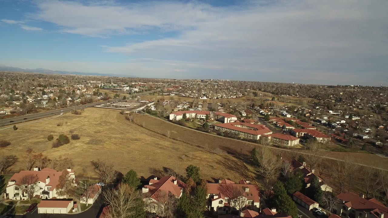 Aerial view over dry field, red-roofed buildings, roads, and suburban homes