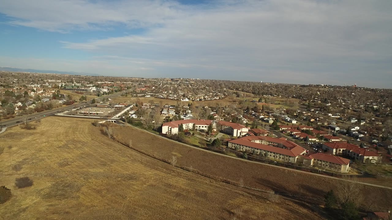 Aerial suburban landscape with fields, houses, roads, and low clouds.