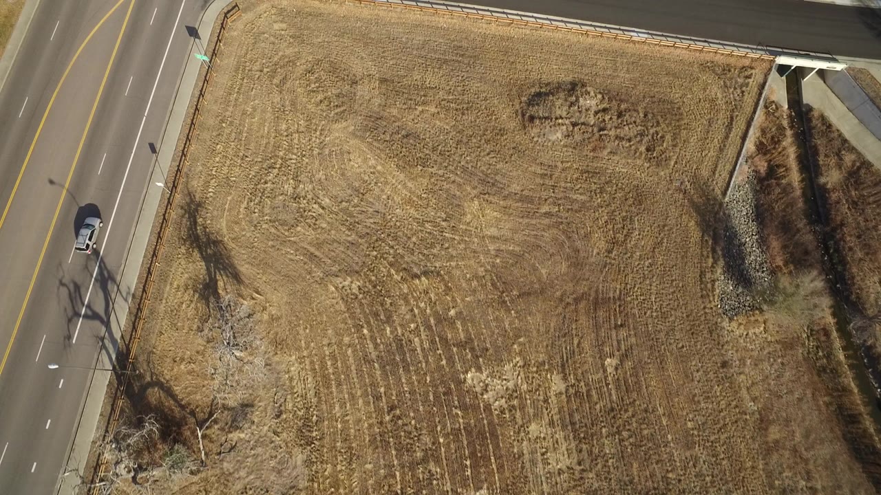Aerial view of a road beside a dry open lot with a car at the left edge.