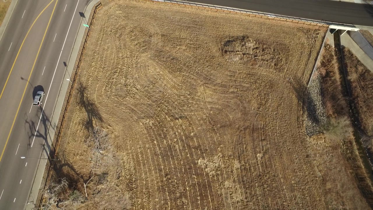 Aerial view in Westminster, Colorado with the dry field filling most of the frame, a road along the left side, a vehicle farther along the lane, and no visible people.