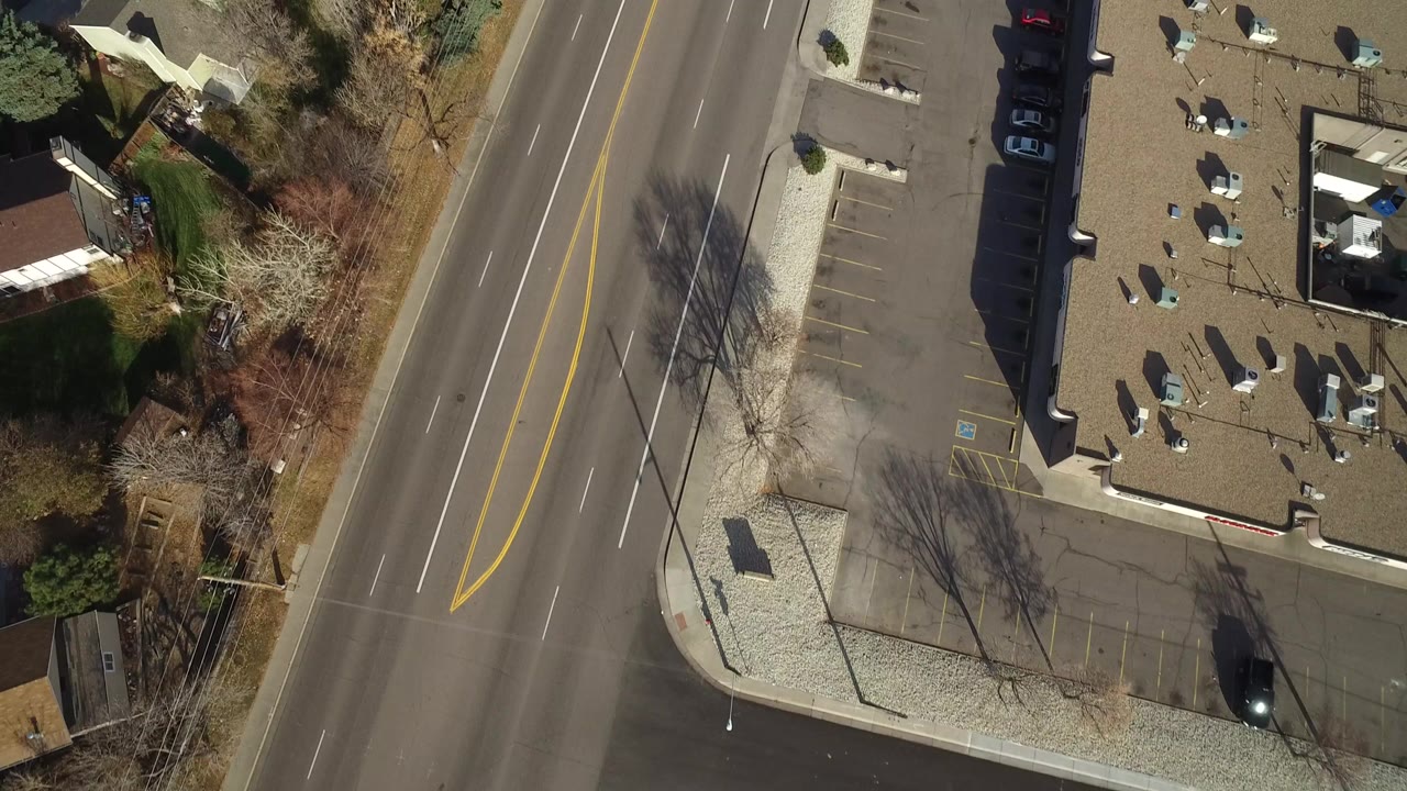 Overhead view of a divided road beside parking lots and small buildings.