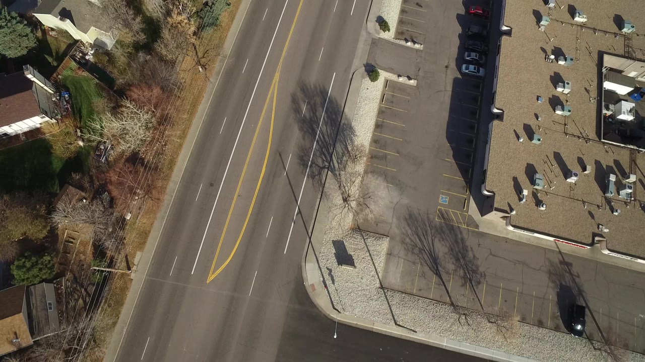 Overhead Westminster, Colorado frame showing the divided roadway next to empty parking spaces, rooftops, bare trees, and no visible people.