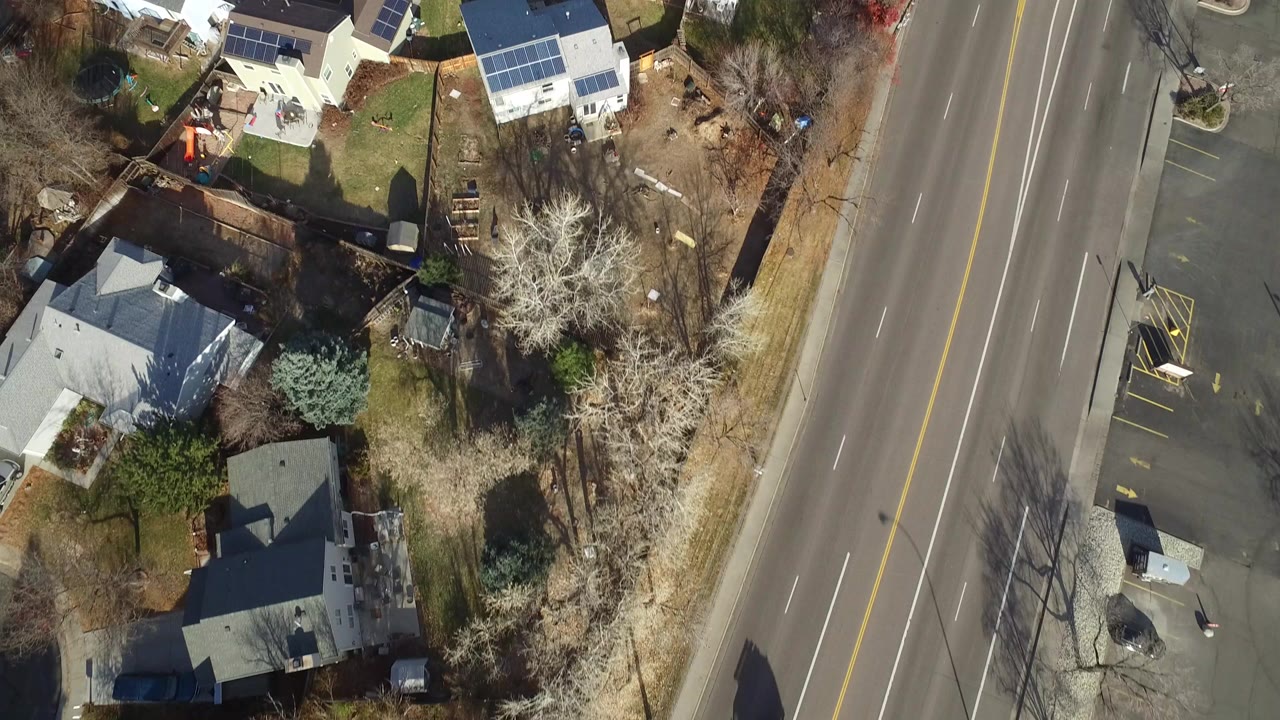 Vertical aerial view over Westminster, Colorado homes, yards, leafless trees, and a multi-lane road at the right edge, with no visible people.