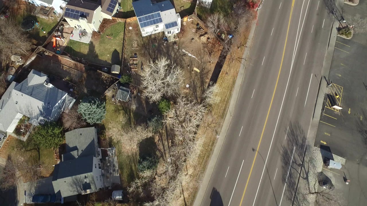 Top-down Westminster, Colorado view with houses clustered left of a multi-lane road, roof solar panels, bare trees, and no visible people.