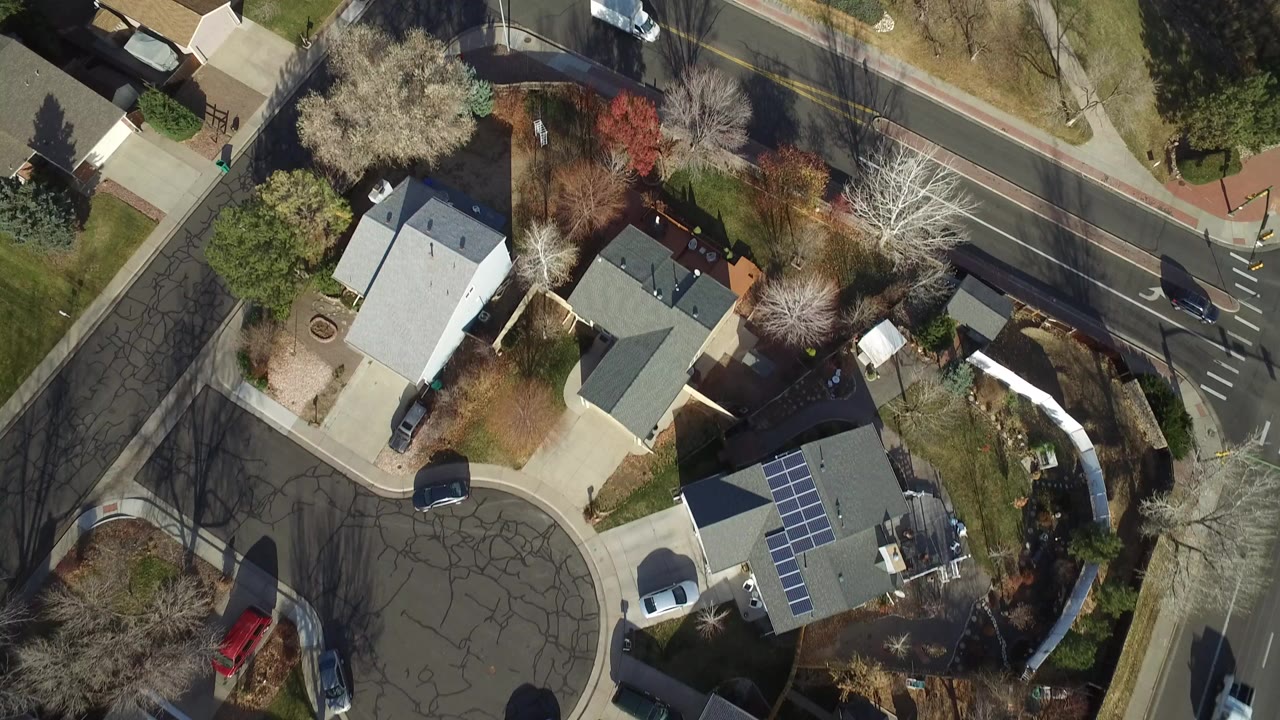 Top-down aerial frame over Westminster, Colorado homes, driveways, sidewalks, trees, and a curved residential street, with no visible people.
