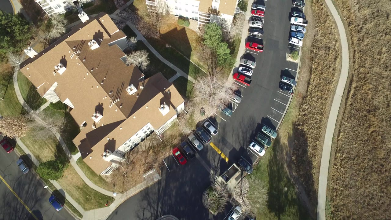 Top-down suburban buildings with parked cars on a curved road and open land nearby.