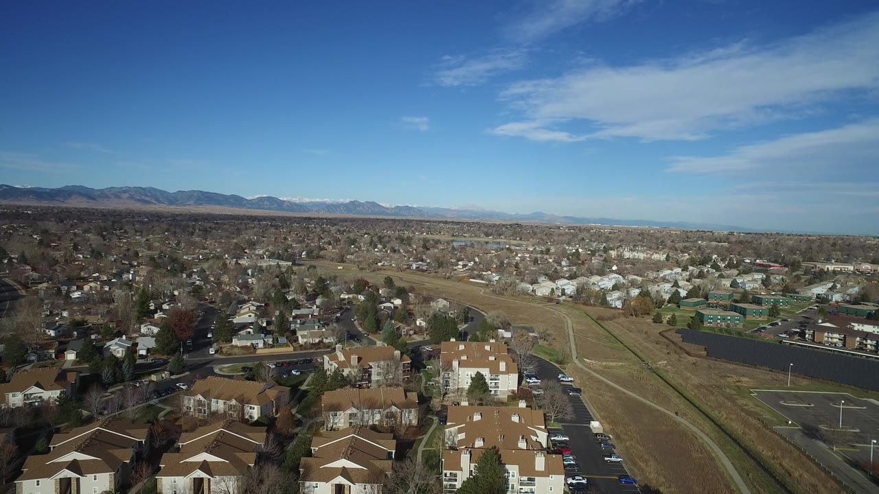 Aerial view in Westminster, Colorado showing the open corridor more centrally, with residential blocks on both sides, a parking lot at lower right, mountains in the distance, and no visible people.