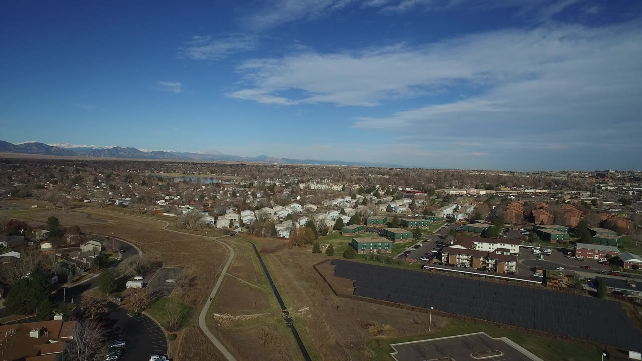 Aerial view over suburban buildings, open land, roads, and distant mountains.