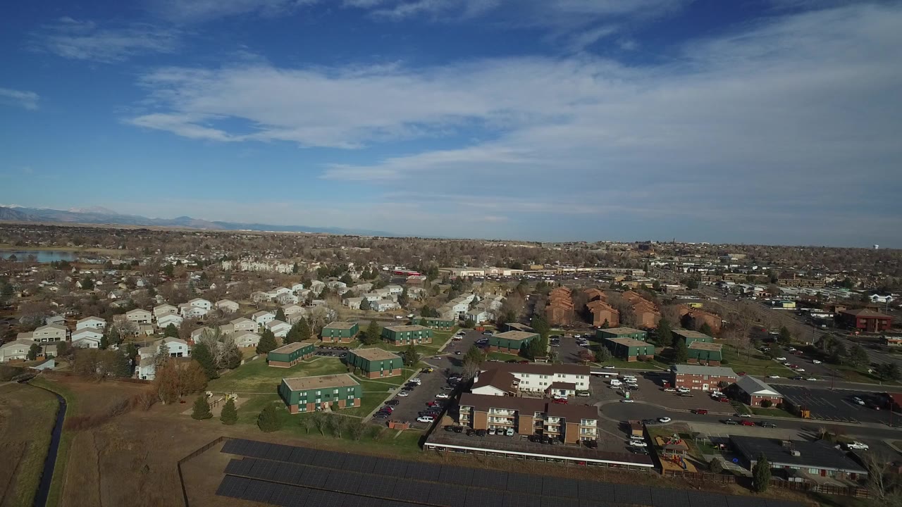 Wide aerial view over suburban homes and apartment buildings under a blue sky.