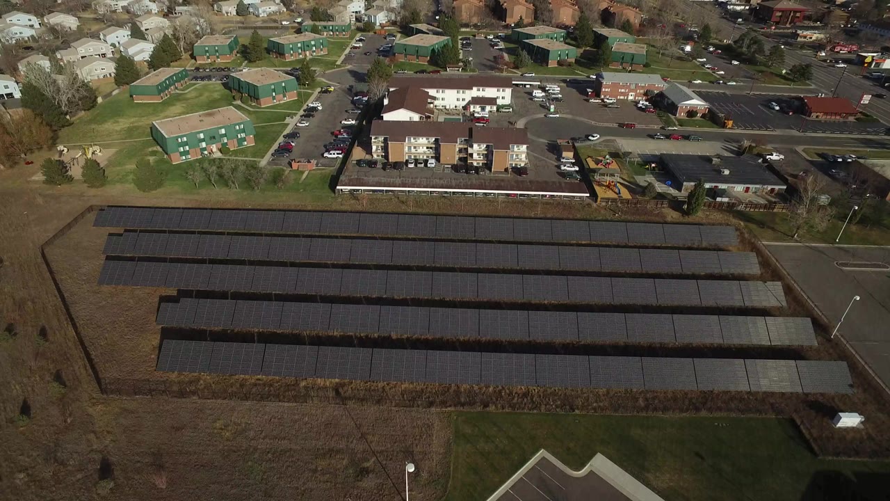 Aerial view of solar panel rows beside roads and low buildings.