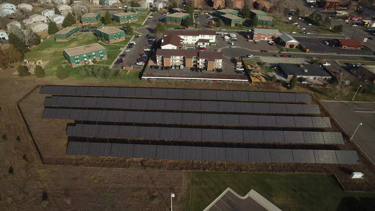 The second frame keeps the Westminster solar array centered, with dark panel bands running horizontally across the field and apartment blocks, parked cars, and neighborhood roofs at the top, no visible people.