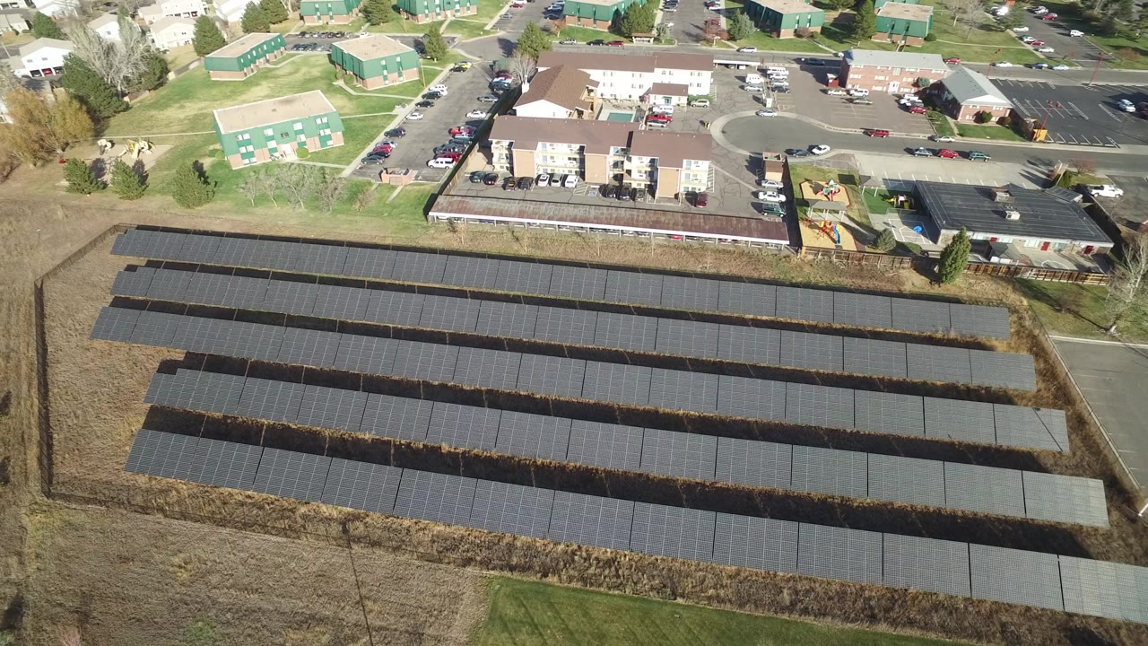 Drone-like view of a solar field with nearby buildings, roads, and a small playground.