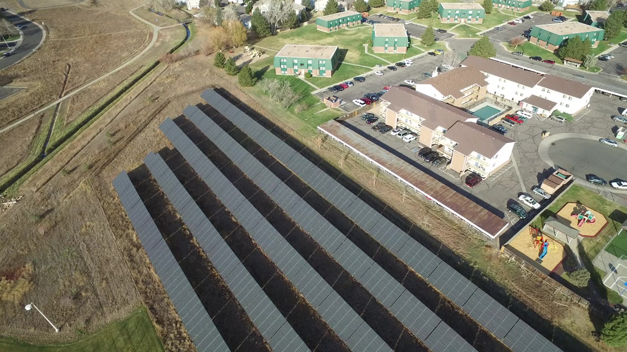 Aerial view of solar panel rows beside buildings and a playground.