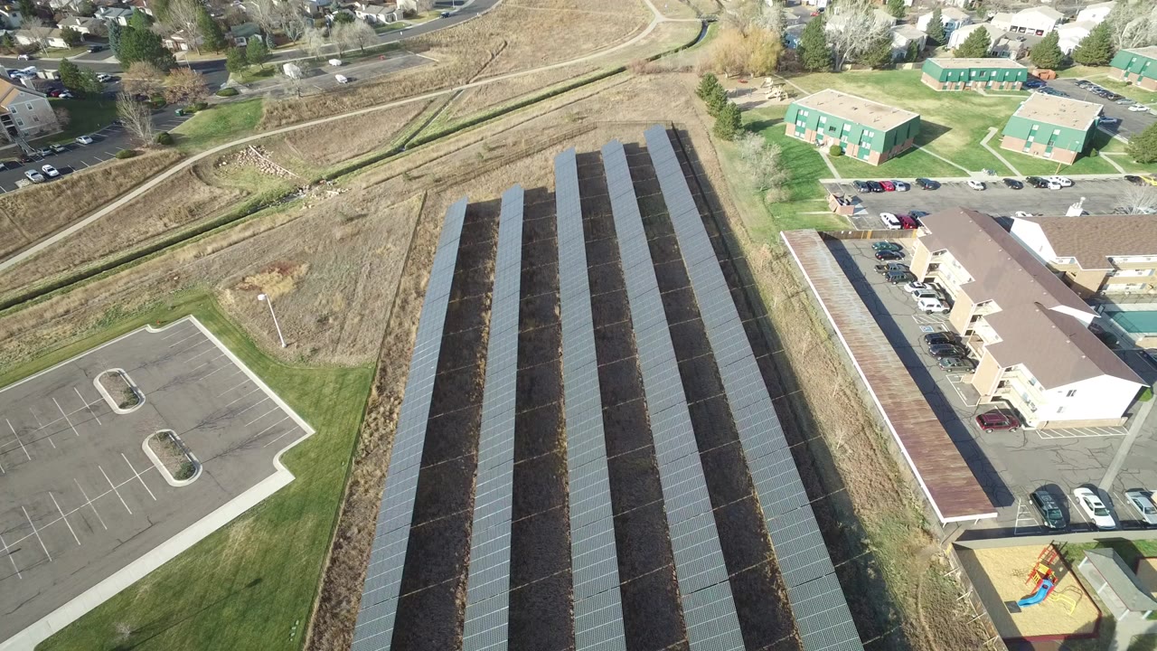 Aerial view of long solar-covered rows beside parking and low buildings.