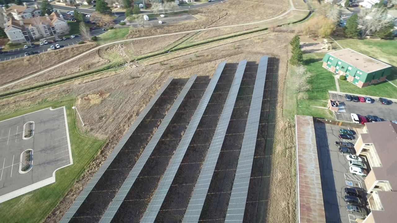 Aerial view of dark panel rows beside a parking lot and grass.