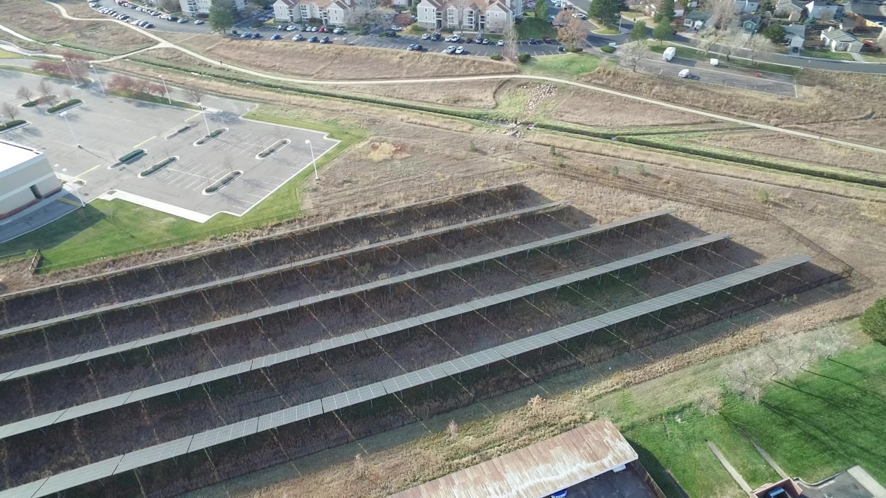Second frame shifts slightly over the Westminster parking area, keeping the white building edge, paved lot, dry open ground, terraced drainage slopes, distant road, and no visible people in view.