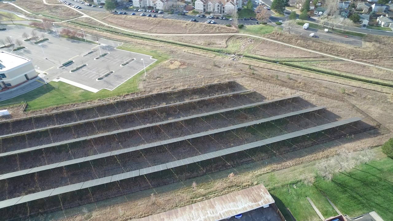 Oblique aerial frame of a mostly empty lot, roadway, open grass, and stepped dark embankments.