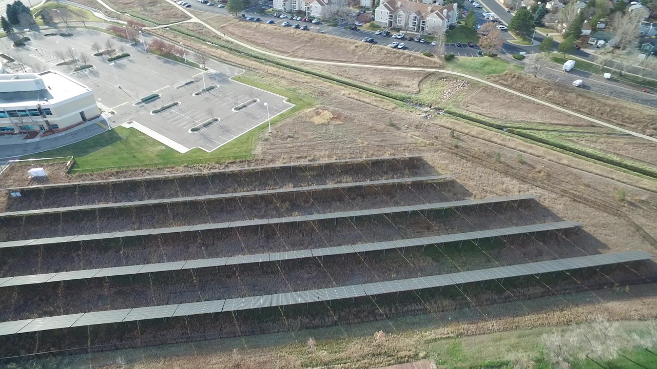 Aerial view of solar panel rows beside a parking lot and buildings.