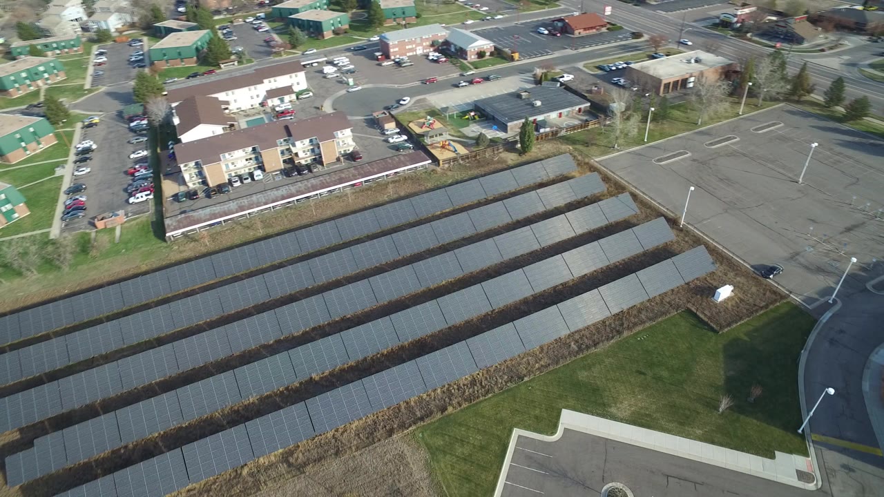 Aerial view of solar panel rows beside apartments and roads.