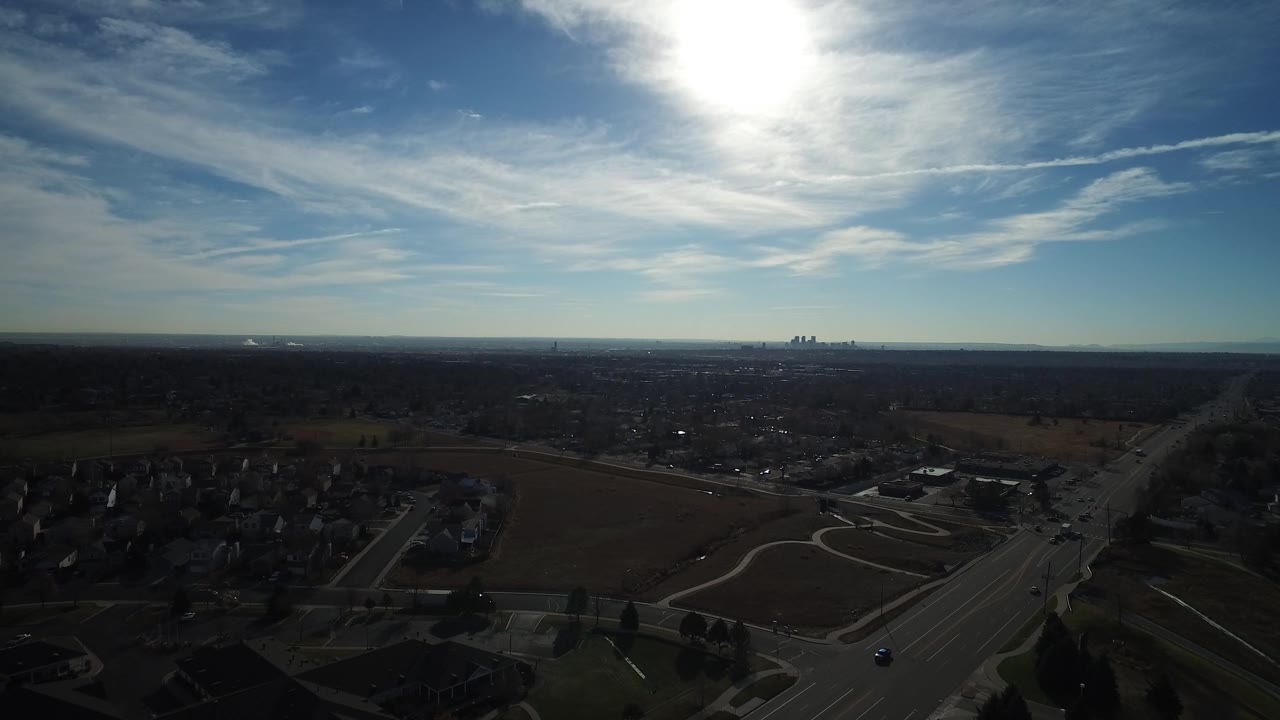 High view across neighborhoods, fields, and a far skyline in harsh sun.