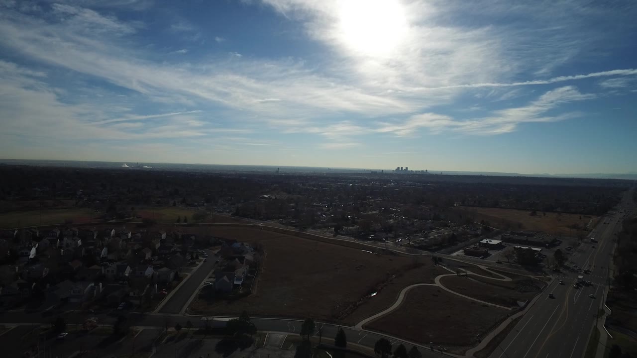 Aerial view of suburban houses, fields, roads, and bright sky glare.