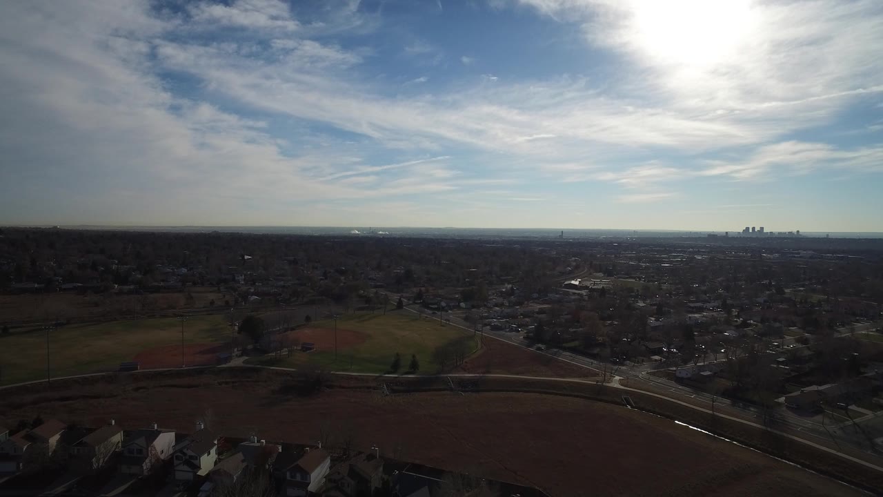 Aerial view of suburbs, fields, roads, and bright sun over a distant skyline.
