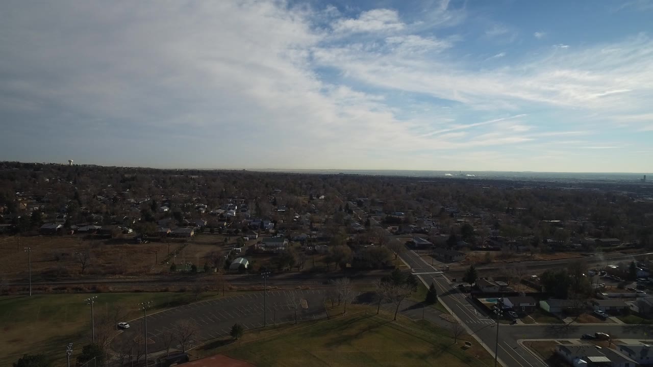 Suburban aerial view with athletic fields, roads, cars, and a large sky.