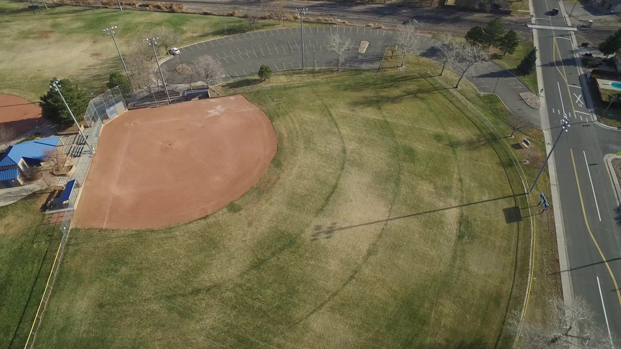 Empty ballfield seen from above with parking lot and road beyond the grass.