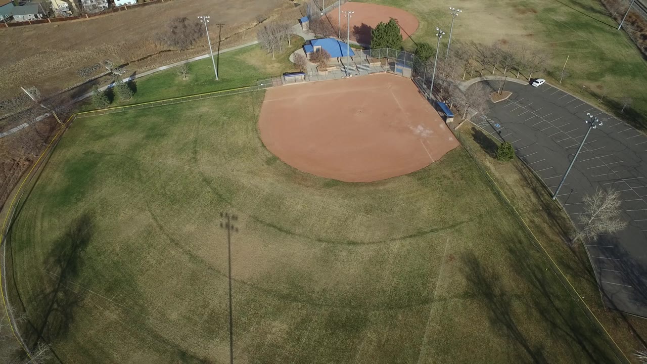 Aerial frame over Westminster, Colorado showing the red dirt infield near the top, broad outfield grass below, park paths and fencing, with no visible people.