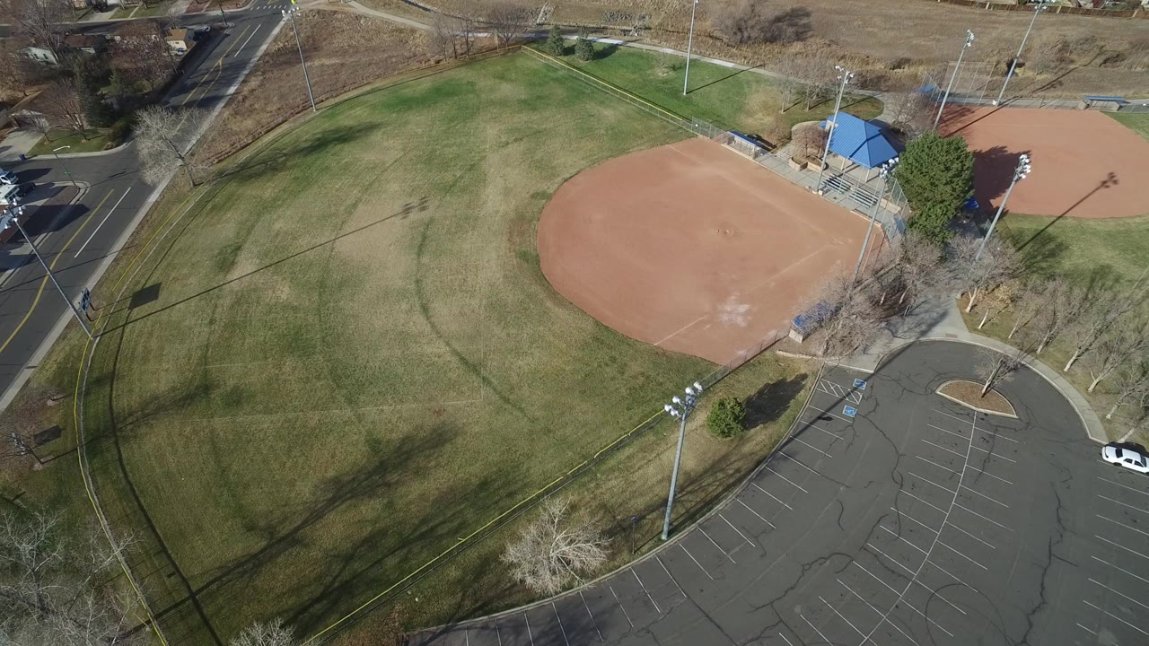 Aerial view of a baseball field beside grass and a parking lot.