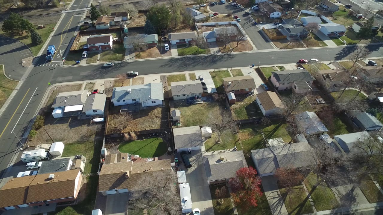Aerial view in Westminster, Colorado showing rooftops, rectangular yards, a broad road through the upper frame, parked cars, and winter-bare trees, with no visible people.