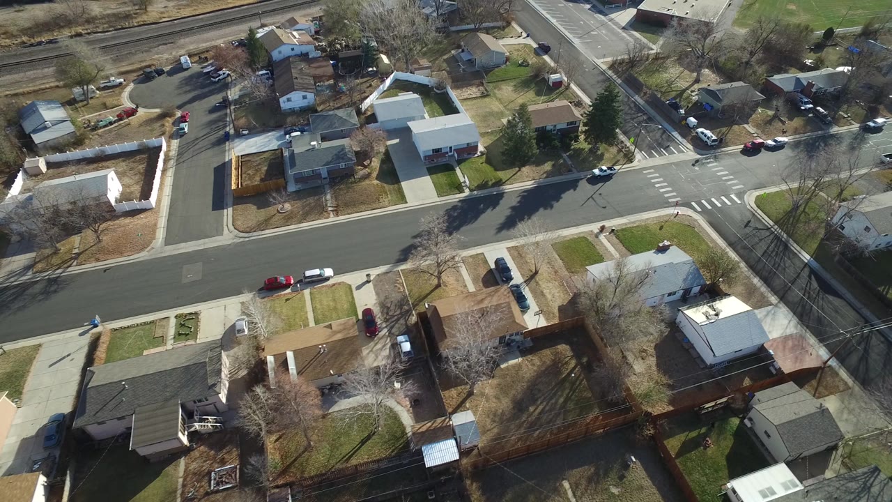 Aerial neighborhood view with houses, yards, streets, and long tree shadows.