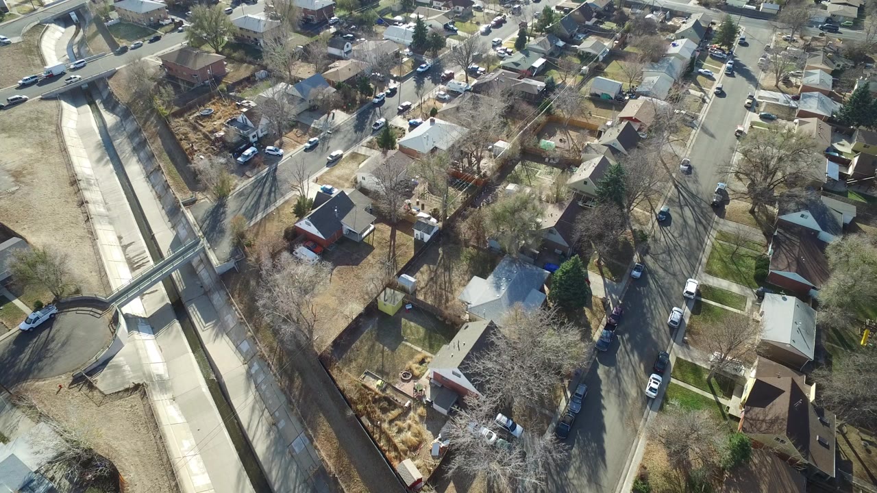 Aerial view of suburban homes, streets, cars, trees, and a concrete channel.