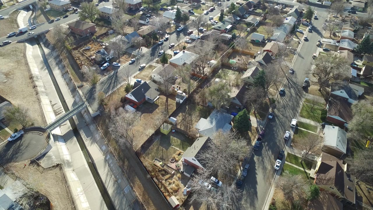 Aerial view in Westminster, Colorado with rooftops, small yards, a street lined with vehicles, and the concrete channel still prominent on the left side.