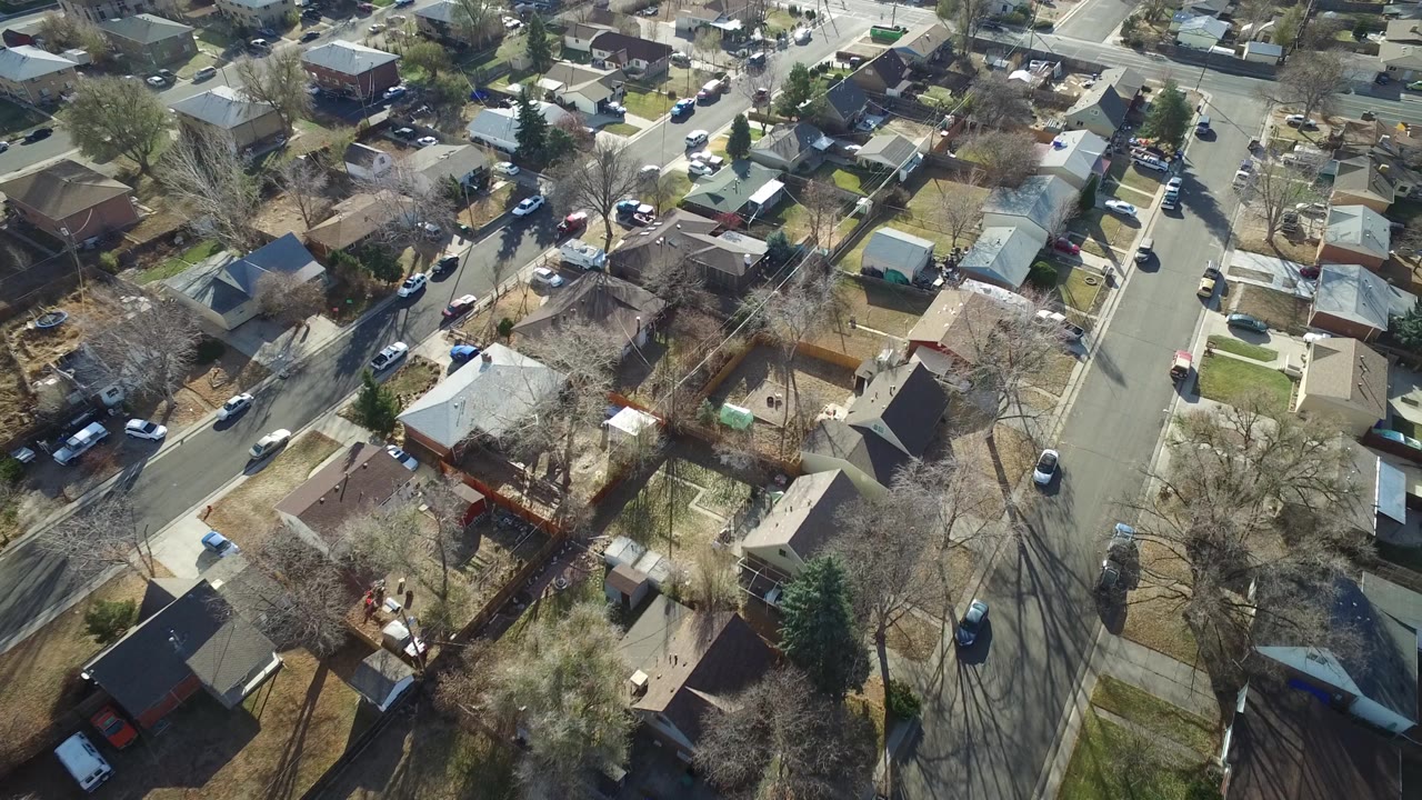 Aerial view in Westminster, Colorado showing detached houses, backyard fences, bare trees, driveways, and cars lining a residential street with no visible people.