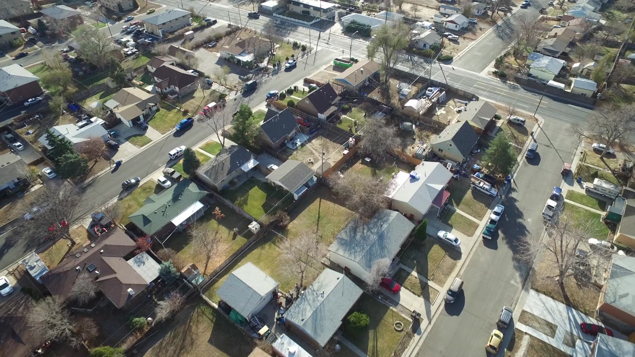 Aerial view in Westminster, Colorado with a broad road near the top of frame, small homes below it, driveways, parked vehicles, bare trees, and no visible people.