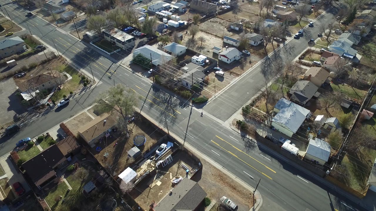 Aerial view in Westminster, Colorado with the main road crossing the lower frame, a side street at right, small houses, yards, parked cars, and no readable faces.