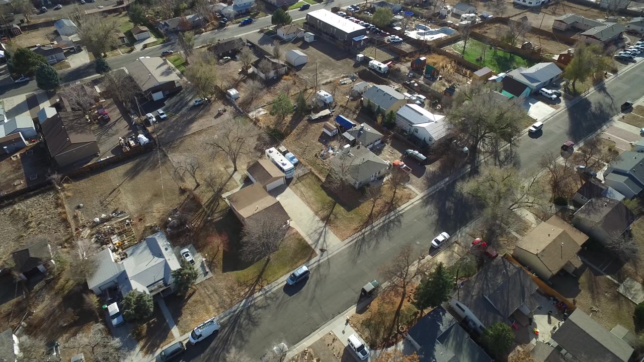 Aerial frame over Westminster, Colorado rooftops and yards, with a broad street cutting through the lower half and no visible people.