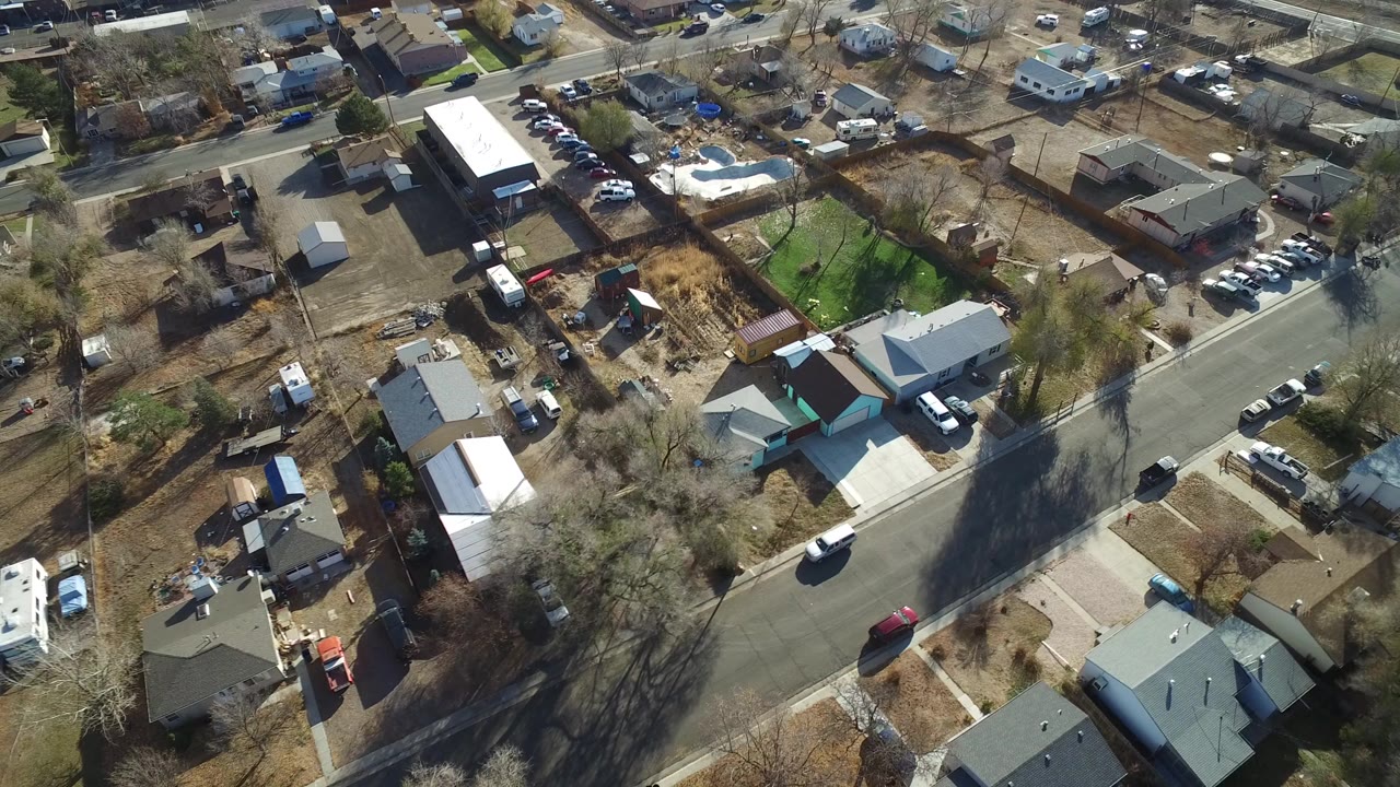 Aerial view over a Westminster, Colorado residential block with single-family homes, fenced yards, bare trees, parked vehicles, and no clearly visible people.