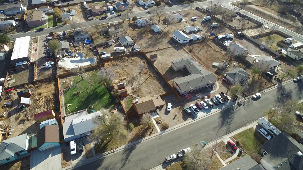 High aerial view in Westminster, Colorado showing a street intersection near the top of frame, rows of houses, driveways, fenced lots, parked vehicles, and no visible people.