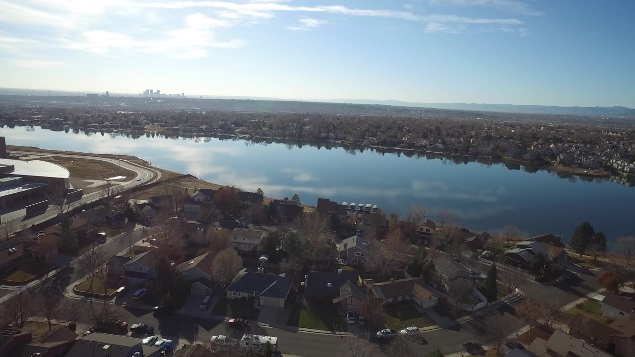 Aerial view in Westminster, Colorado showing large buildings and roads at the water's edge, residential blocks below, reflective blue water, and no visible people.