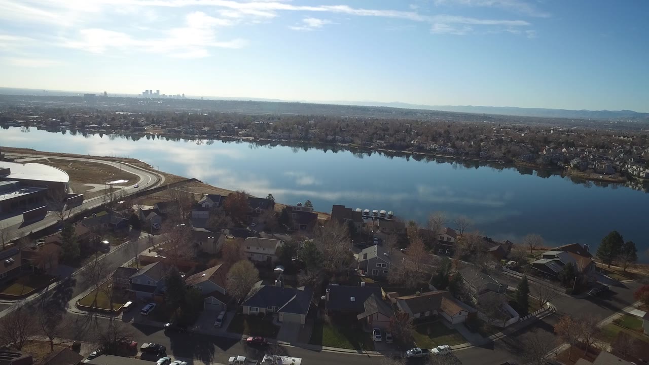 Wide aerial over a water body dividing neighborhoods and distant city buildings.