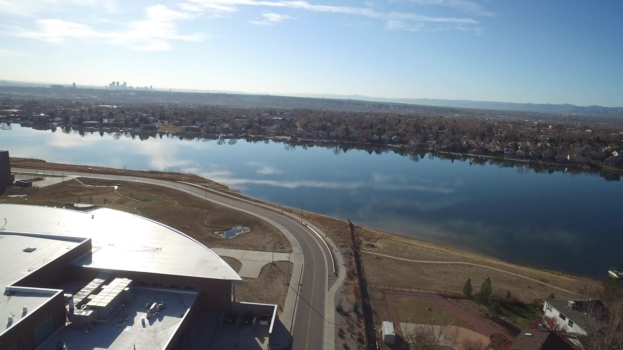 Aerial view with warehouse roof corner, curved road, lake, and far city skyline.