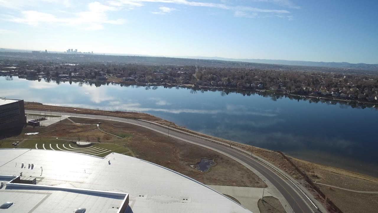 Aerial view of a lake, road, rooftop, and distant city skyline.